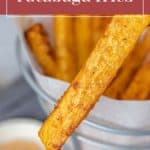 Close-up of a hand holding a seasoned rutabaga fry with more delicious rutabaga fries in a serving container below. Text overlay reads, "Spiced Rutabaga Fries.