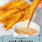 A hand dips a roasted rutabaga fry into a creamy sauce while more delicious rutabaga fries rest on a parchment sheet in the background. Text on the image reads "stetted.com Roasted rutabaga fries.