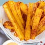 Close-up of oven-baked rutabaga fries in a paper cone, accompanied by a dipping sauce. The text "rutabaga fries" is prominently displayed at the top of the image.