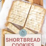 A tray of easy shortbread cookies, freshly cut and resting on parchment paper, sits atop a wooden cutting board.