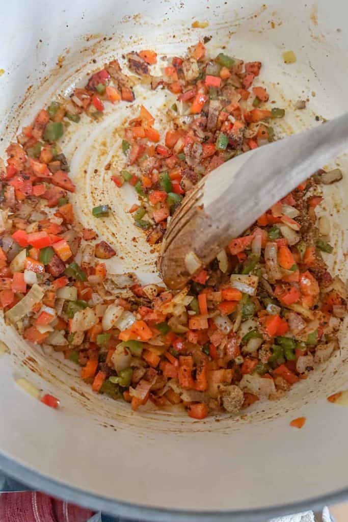 Wooden spoon stirring sauteed vegetables with spices.