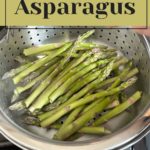 Steamed asparagus in a metal colander on a stove, illustrating the perfect method for how to cook asparagus. A text overlay reads "How to Cook Asparagus.