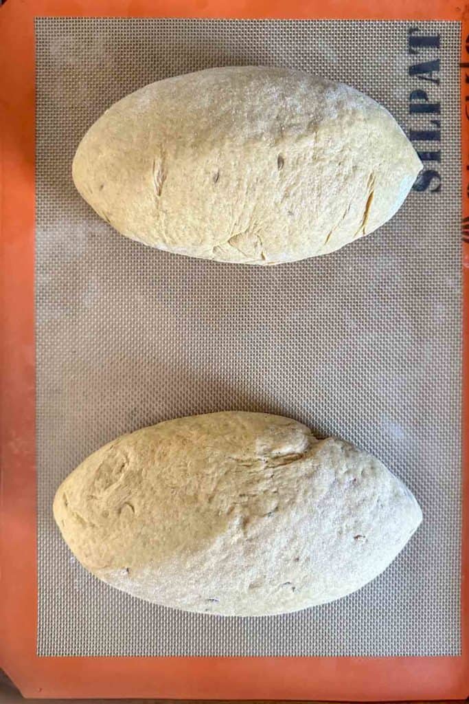 Unbaked shaped limpa bread loaves on a lined baking sheet.