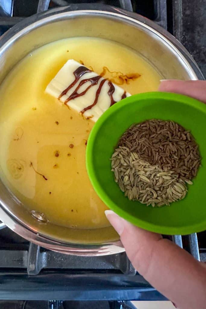 Saucepan filled with orange juice, butter, molasses, and brown sugar with seeds being added.