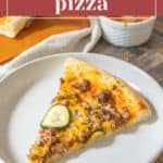 A slice of cheeseburger pizza, laden with savory toppings, sits invitingly on a plate, set against the backdrop of a delectable whole pizza and rich sauce.