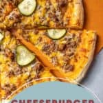 Served on an eye-catching orange surface, this cheeseburger pizza is topped with sliced pickles and flavorful ground meat on a perfectly baked crust.