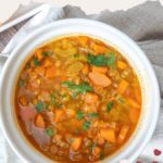 A bowl of hearty red lentil soup with carrots and herbs sits on a light tablecloth. Text reads: "Easy to make, this red lentil soup is a must-try. Get the recipe at stetted.com".