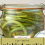 A glass jar filled with pickled garlic scapes sits elegantly, adorned with a charming blog name label.