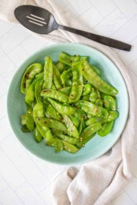 Overhead of sautéed snow peas on a blue plate.