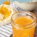 A jar of homemade peach jam sits on a wooden surface. In the background, a biscuit generously topped with peach jam is visible. The text "homemade peach jam" graces the top, while "stetted.com" is elegantly displayed at the bottom.