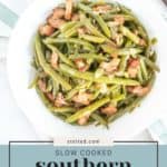 A white bowl of southern green beans slow-cooked with savory bacon pieces rests on a light-striped cloth.