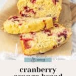 A loaf of cranberry orange bread is partially sliced on a piece of parchment paper. The text below reads "cranberry orange bread - quick and easy recipe".