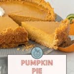 A pumpkin pie with a graham cracker crust is shown, with one slice being lifted from the pie. A small dollop of cream tops the slice, and a background featuring a pumpkin can be seen. Text reads "Pumpkin Pie with Graham Cracker Crust.