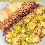 A bowl of roasted Brussels sprout salad with sliced apples, dried cranberries, and pecans.