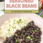 A bowl with white rice and seasoned black beans, garnished with chopped herbs. Text overlay reads: "Delicious Seasoned Black Beans. Get the recipe at stetted.com.