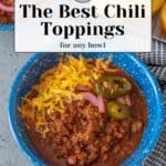 A bowl of chili topped with shredded cheese, jalapeños, and onions sits enticingly. Cornbread is in the background. Text overlay reads, "Discover the Best Chili Toppings for Any Bowl.