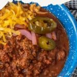 A bowl of chili topped with shredded cheese, pickled jalapeños, and red onions. Text reads "Discover the Ultimate Chili Toppings.