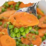 A spoonful of tender peas and carrots, garnished with fresh herbs.