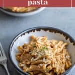 A bowl of creamy french onion pasta garnished with grated cheese and herbs, accompanied by a fork on the side. Another delightful serving of french onion pasta sits invitingly in the background.