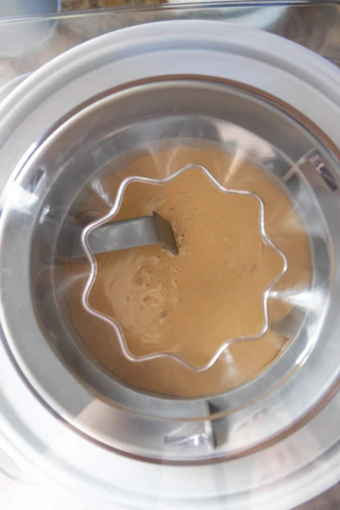 A close-up view of a coffee-colored mixture being churned in an ice cream maker.