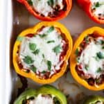 Stuffed bell peppers with melted cheese and chopped herbs in a baking dish.
