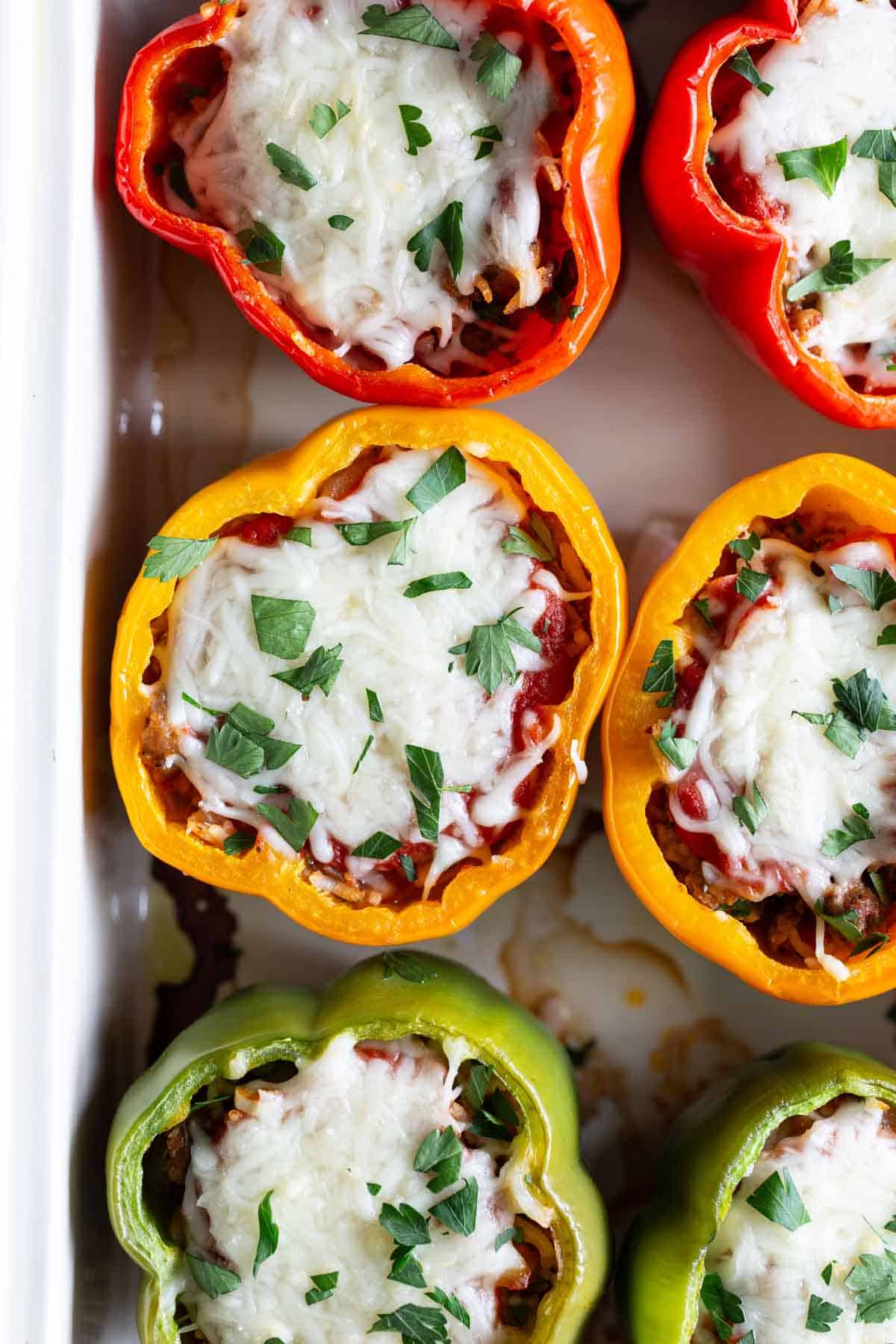Stuffed bell peppers with melted cheese and chopped herbs in a baking dish.
