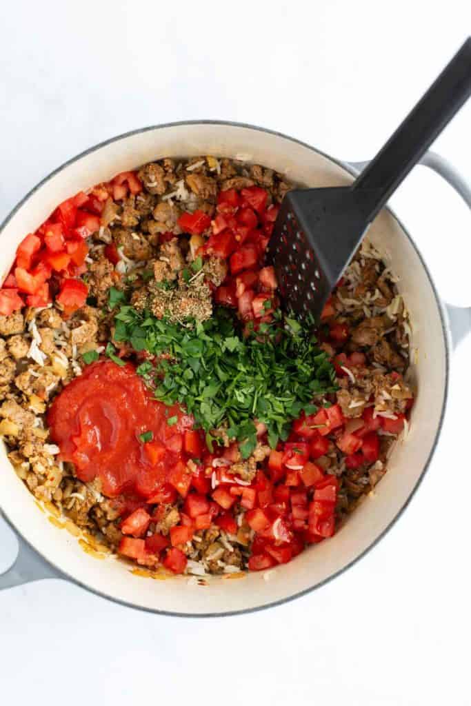 A pot containing rice, ground meat, diced red bell peppers, herbs, and tomato sauce with a black spatula.