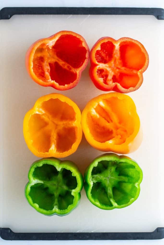 Sliced red, yellow, and green bell peppers arranged in two rows on a white cutting board.