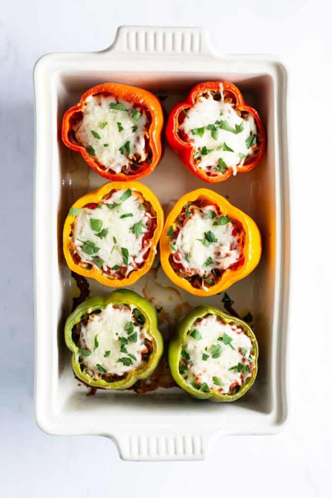 Stuffed bell peppers with cheese and herbs in a baking dish, viewed from above.