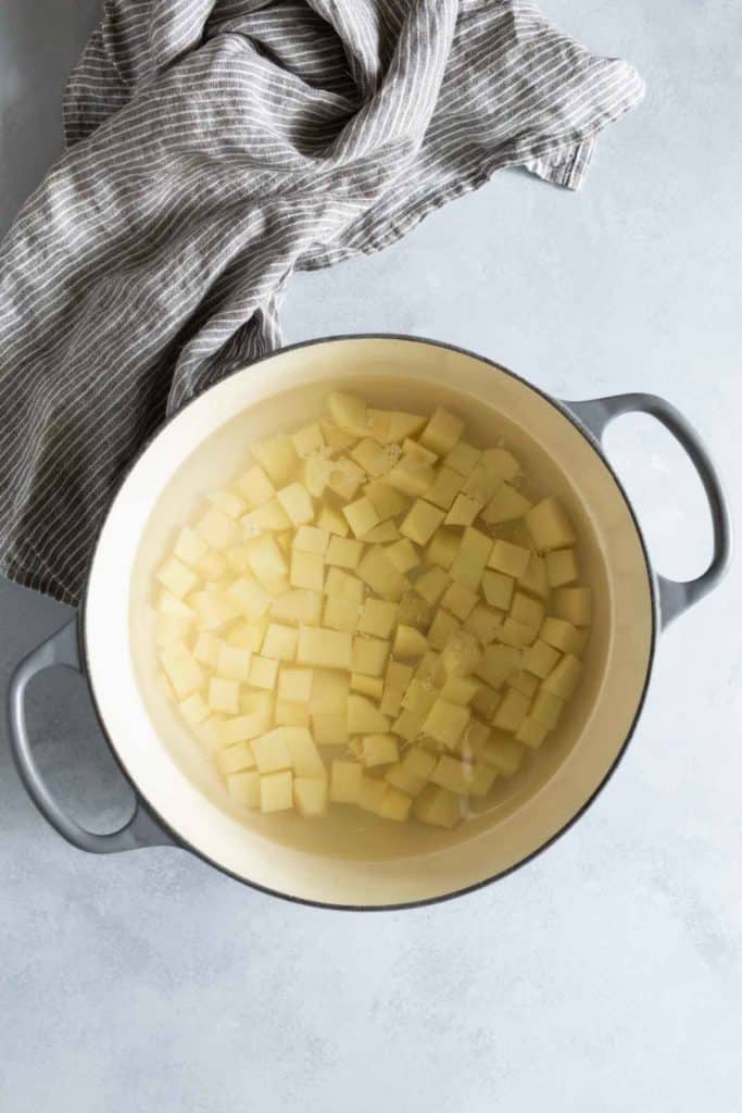 A pot filled with water and cubed potatoes sits on a gray countertop next to a striped kitchen towel.
