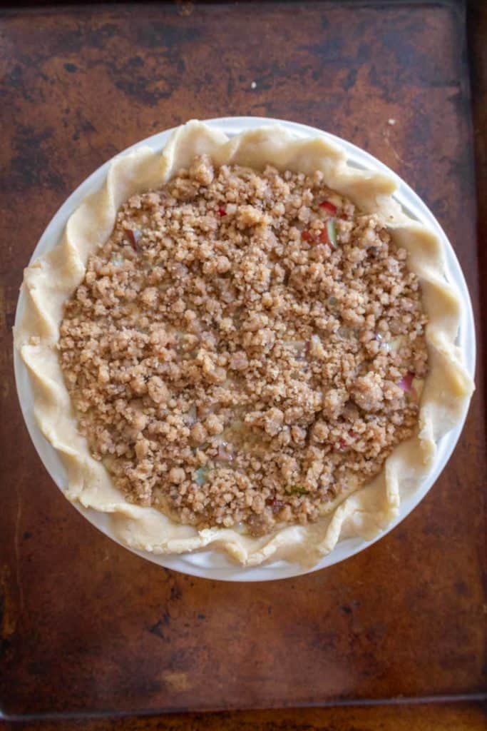 A pie dish filled with an unbaked pie that has a crumb topping, placed on a brown countertop.