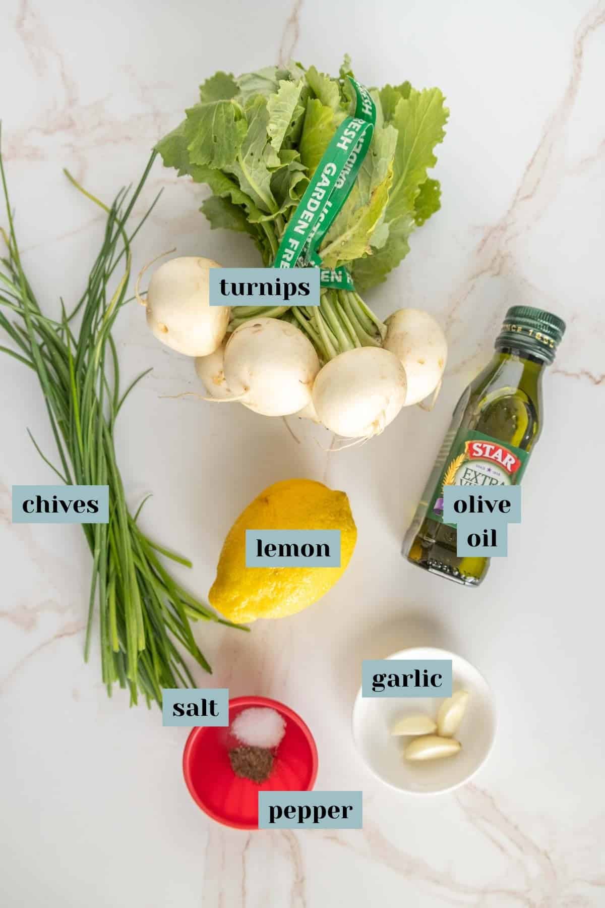 Ingredients arranged on a surface: a bunch of turnips, chives, a lemon, a bottle of olive oil, garlic cloves, and a small dish containing salt and pepper.