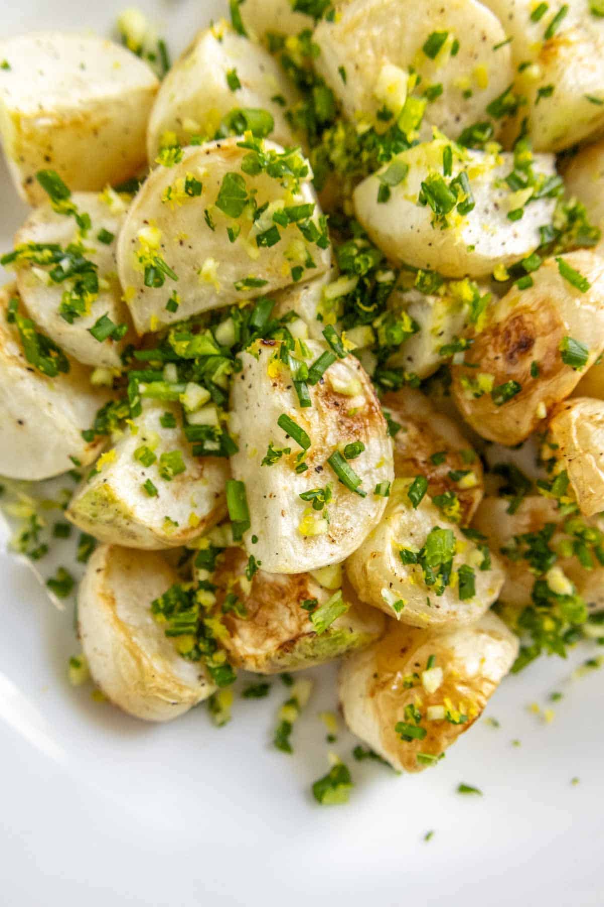 Close-up of roasted diced potatoes garnished with finely chopped herbs, served on a white plate.