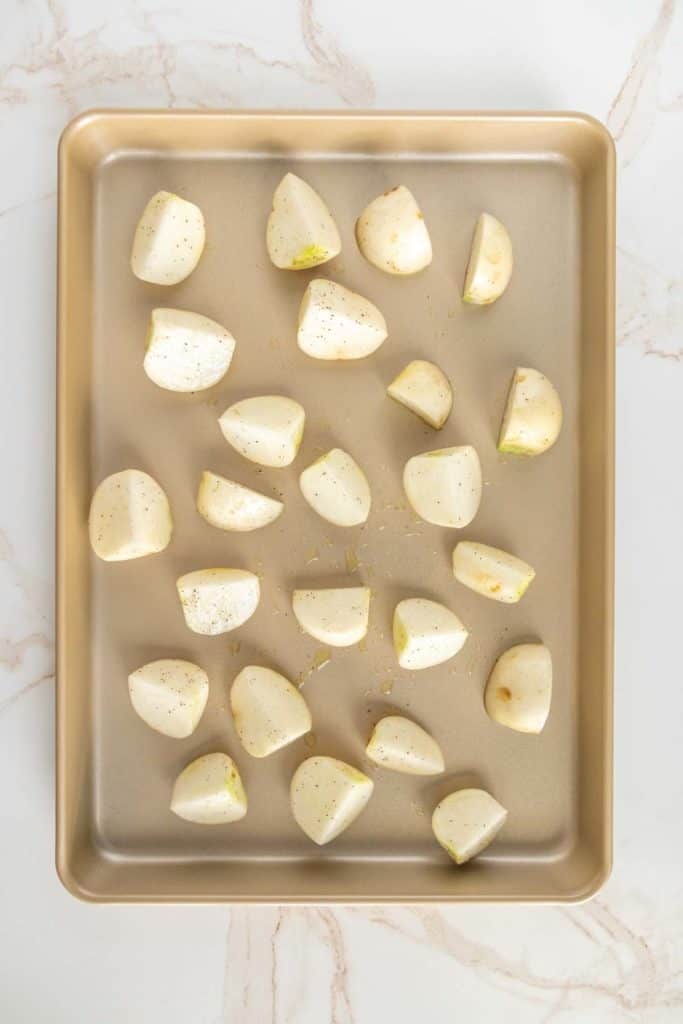 Chopped turnip pieces seasoned with salt and pepper arranged on a baking sheet.