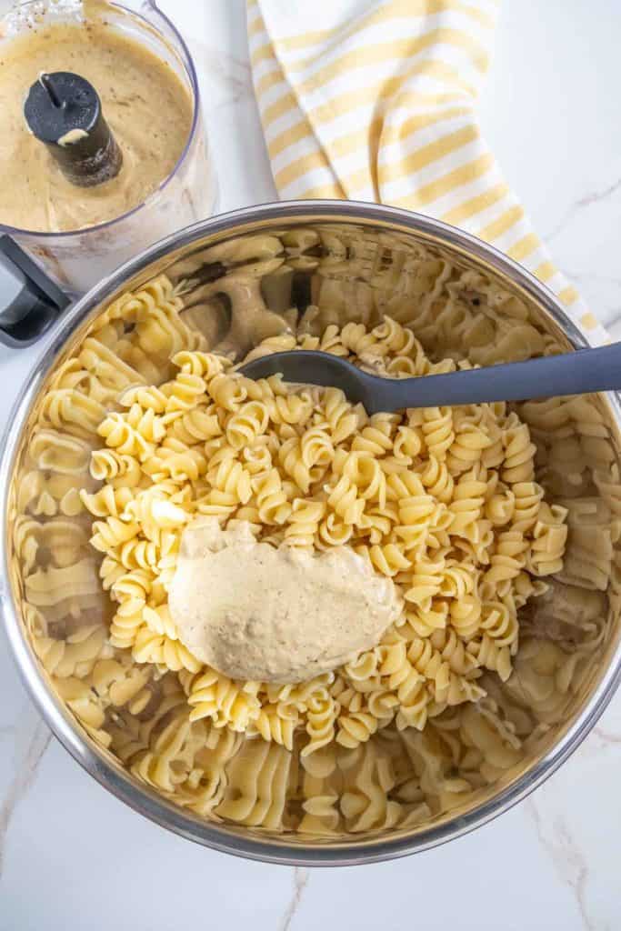 A metal bowl filled with cooked pasta, a dollop of sauce on top, a spoon, and a striped towel in the background.