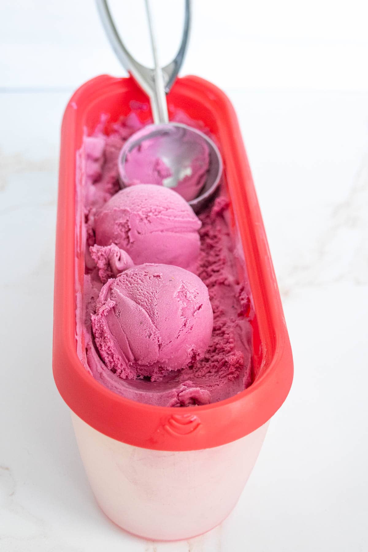 A container of pink ice cream with two scoops on top and an ice cream scoop resting inside.