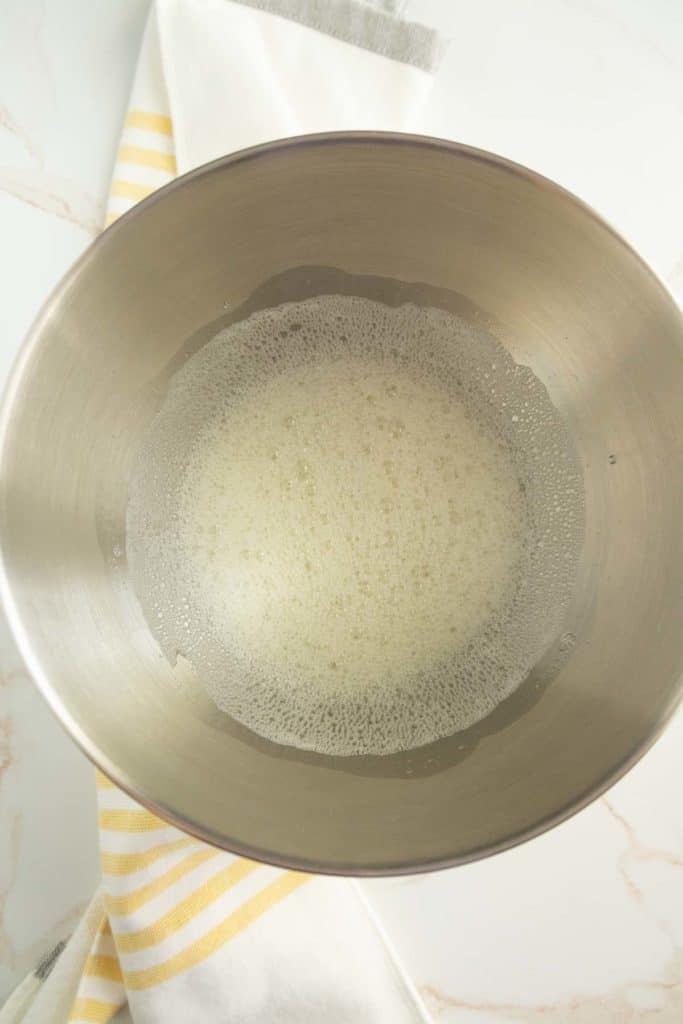 A stainless steel bowl containing lightly foamed beaten egg whites on top of a yellow and white striped kitchen towel.