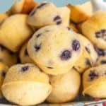 A close-up of several mini blueberry muffins stacked together, displayed against a teal background with the text "mini BLUEBERRY MUFFINS" at the top. Indulge in these bite-sized delights!