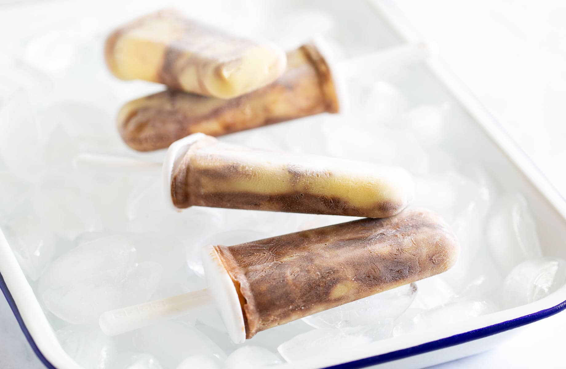 Four swirl-patterned popsicles rest on a tray filled with ice cubes.