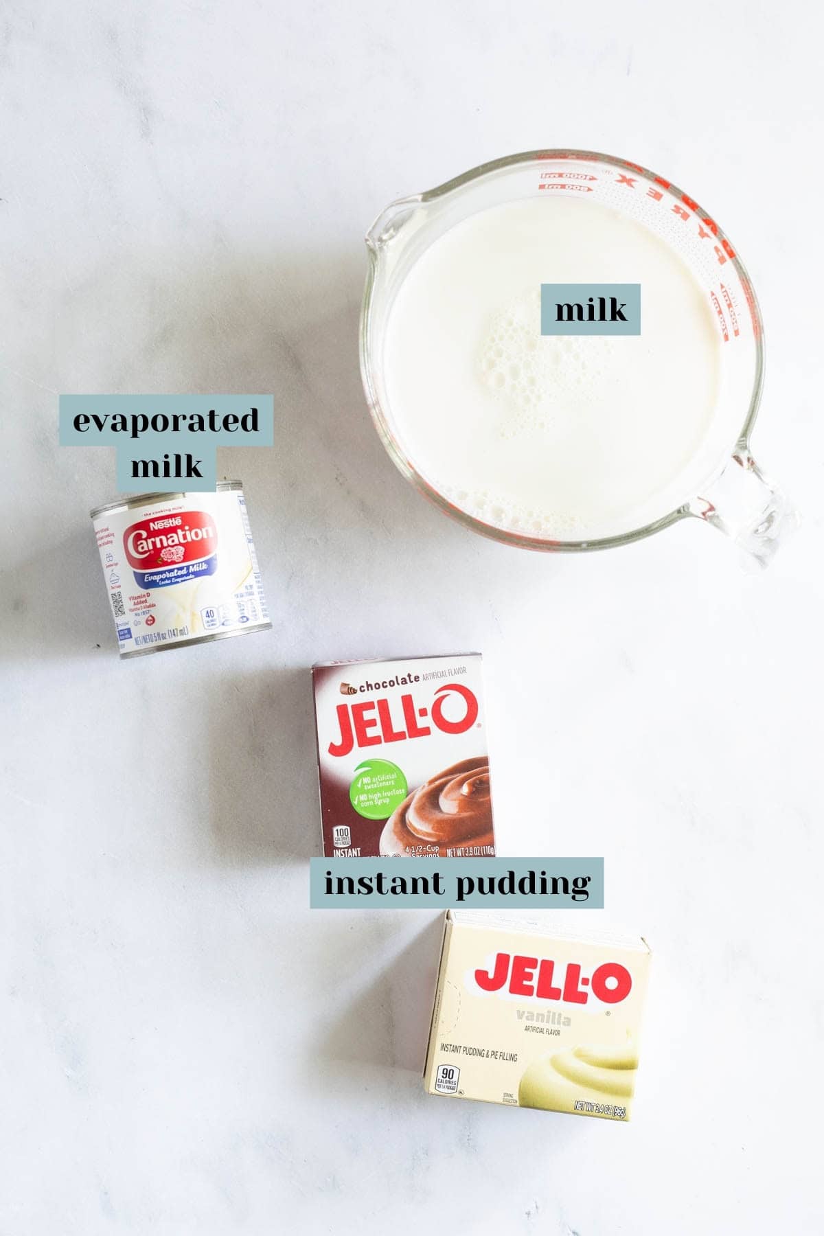 A measuring cup filled with milk next to a can of evaporated milk and two boxes of instant pudding, one chocolate and one vanilla.