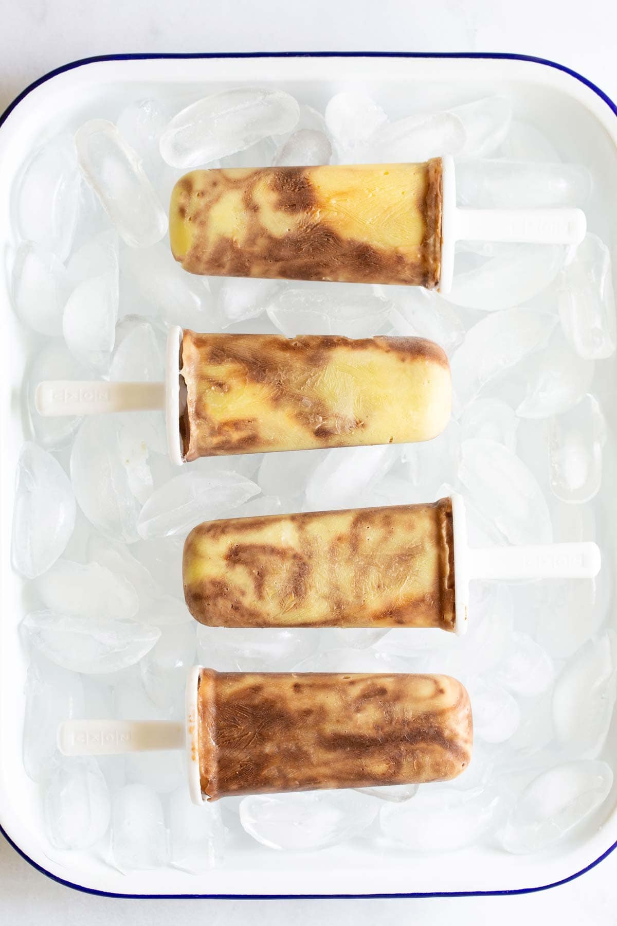 A tray with four chocolate and vanilla swirled popsicles is placed on a bed of ice.