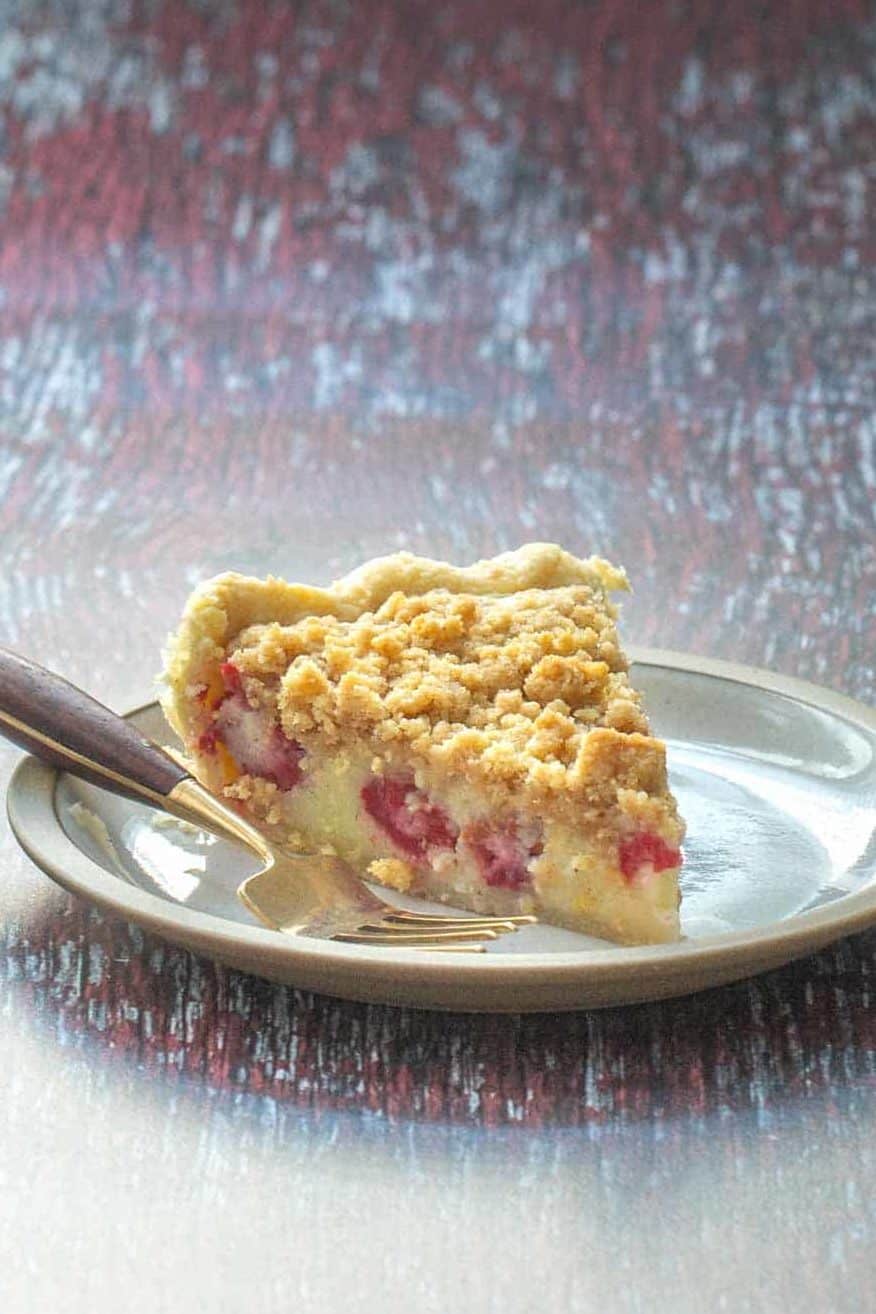 A slice of pie with a crumbly golden crust and visible chunks of fruit on a plate, accompanied by a fork.