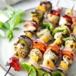 Grilled chicken skewers with bell peppers, onions, and pineapple on a plate, garnished with fresh basil.