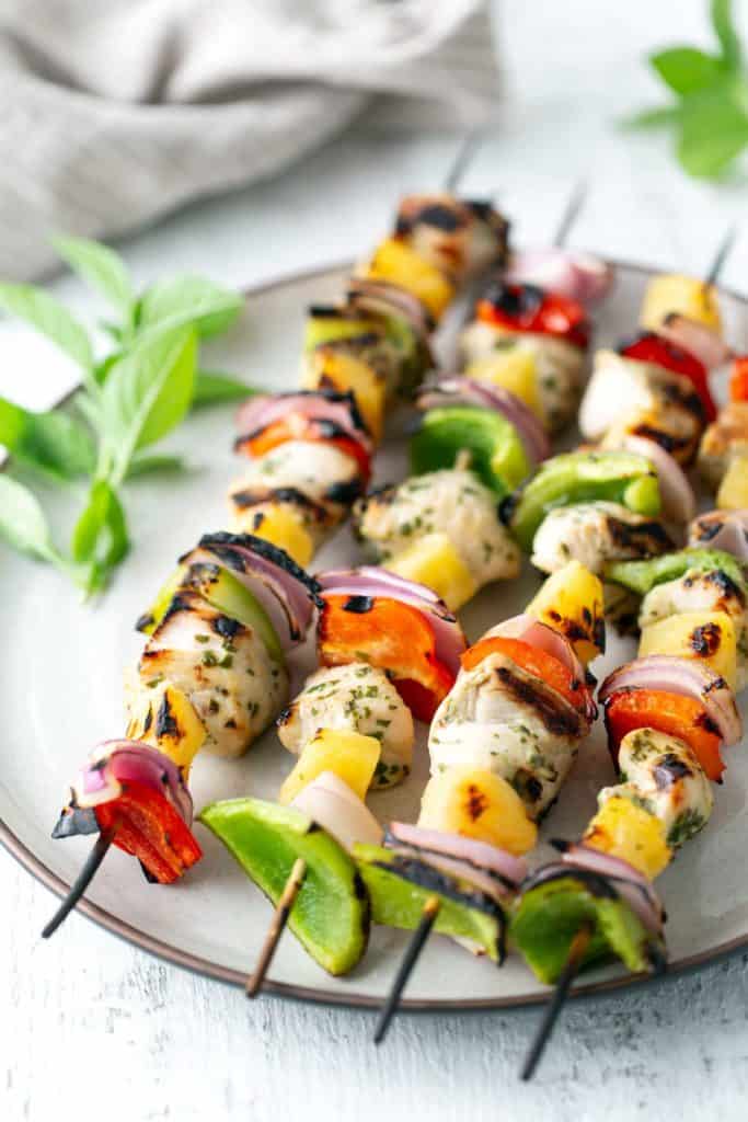 Grilled chicken skewers with bell peppers, onions, and pineapple on a plate, garnished with fresh basil.