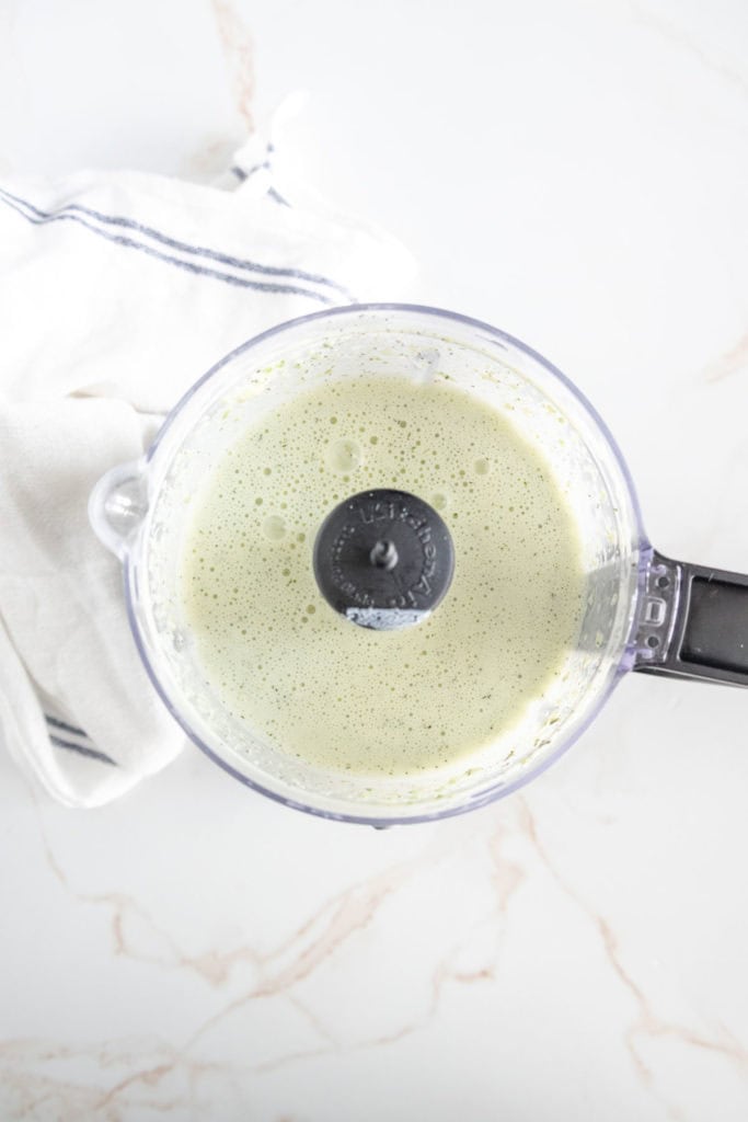 A blender filled with a green smoothie mixture, viewed from above, on a white countertop with a striped cloth beside it.