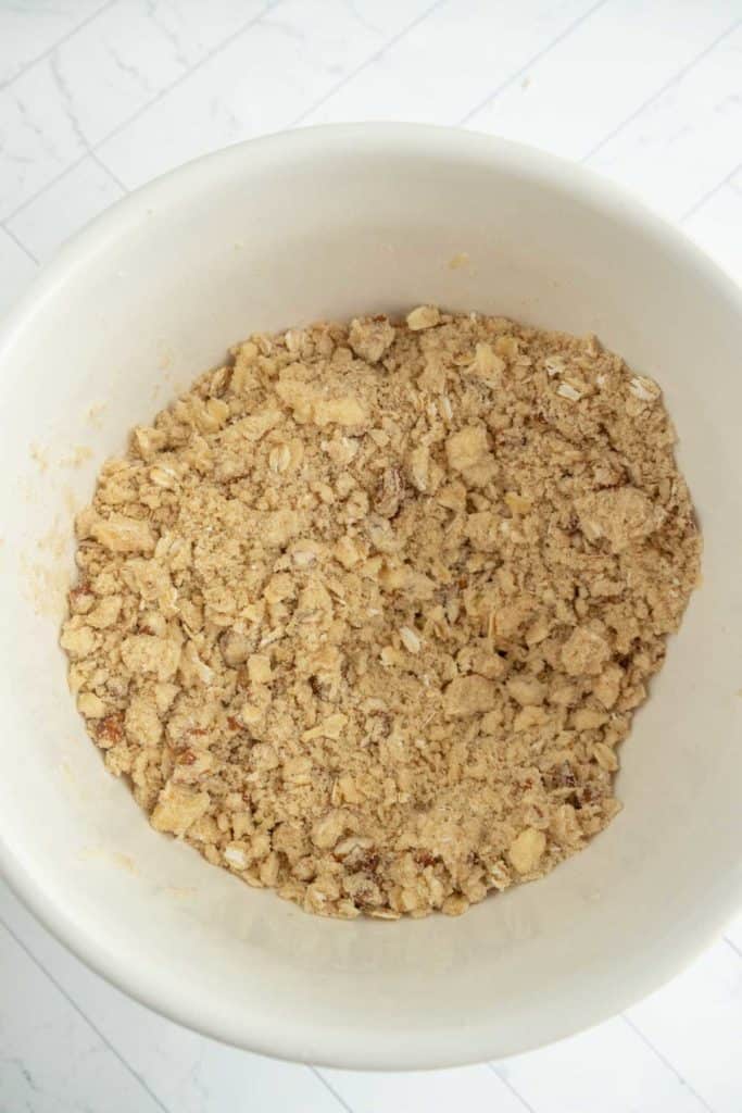 A white bowl containing a mixture of crumbly topping, likely a streusel topping, on a light marble surface.