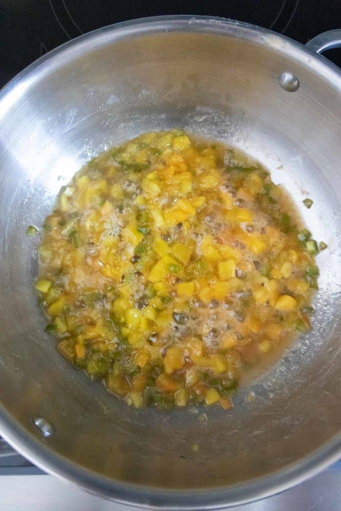 A metal pot on a stovetop containing simmering diced vegetables in a liquid.