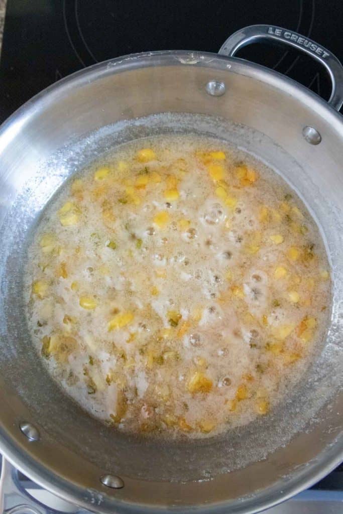 Stainless steel pot on a stove containing a bubbling mixture of corn kernels and seasonings.