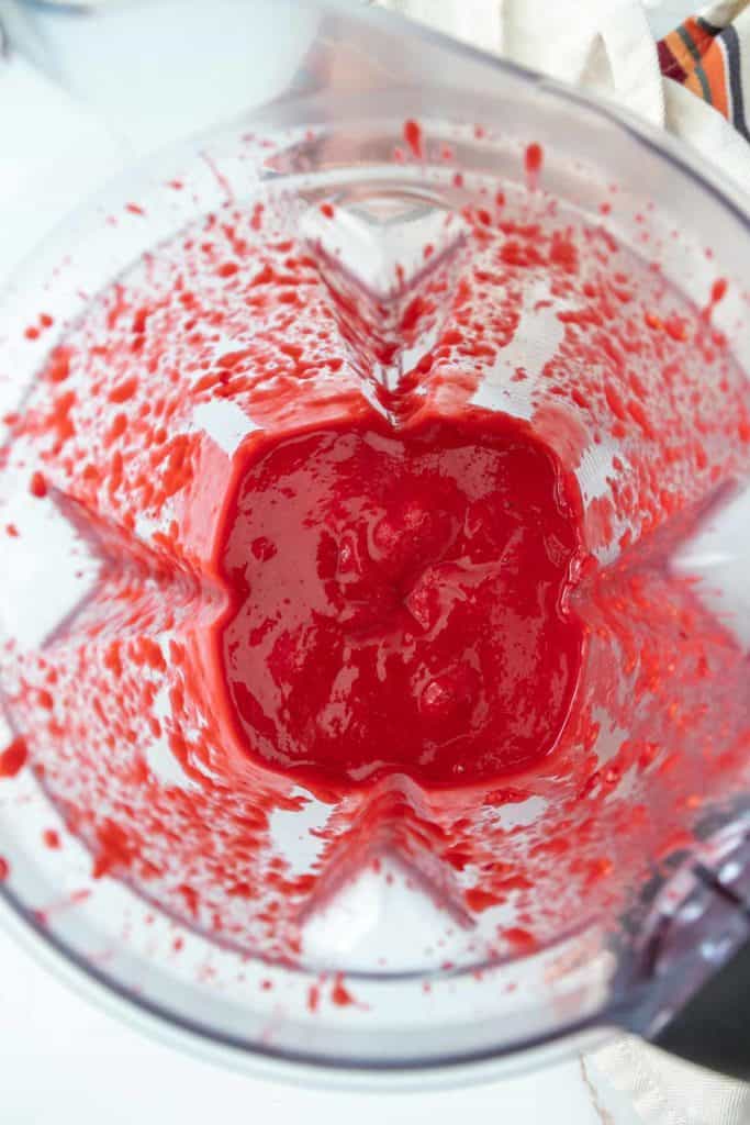 Top view of a blender with a smooth red mixture inside, possibly a fruit or vegetable puree.