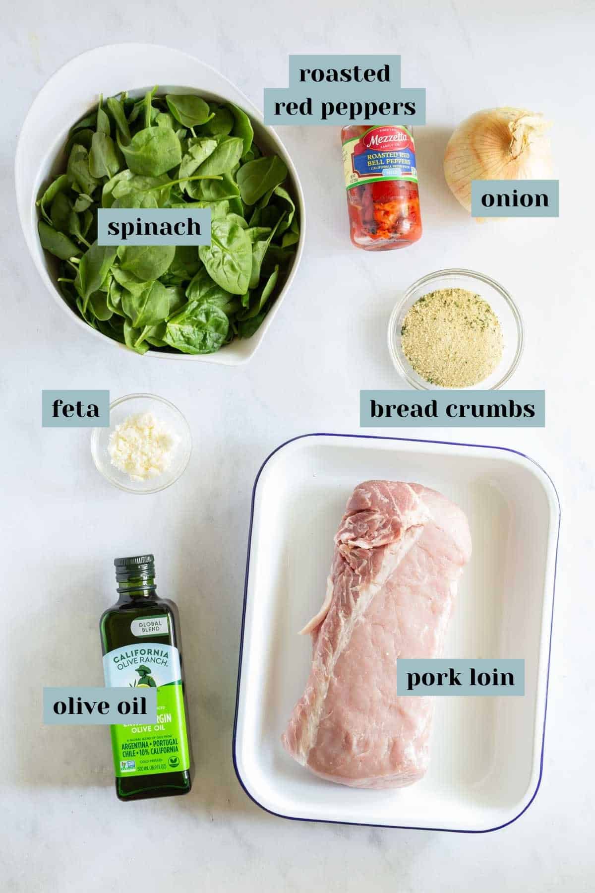 Ingredients for a recipe displayed on a countertop: bowl of spinach, jar of roasted red peppers, onion, feta cheese, bread crumbs, olive oil bottle, and a raw pork loin in a dish.